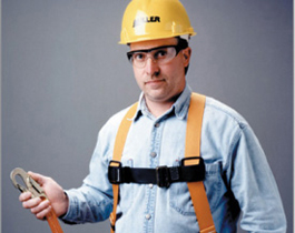 Construction worker wearing a safety harness and hard hat, holding fall protection equipment.